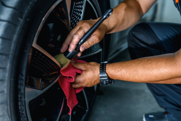 Detailer cleaning a wheel with a brush and cloth